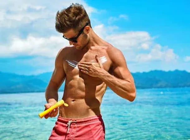 Buff man applying sun lotion